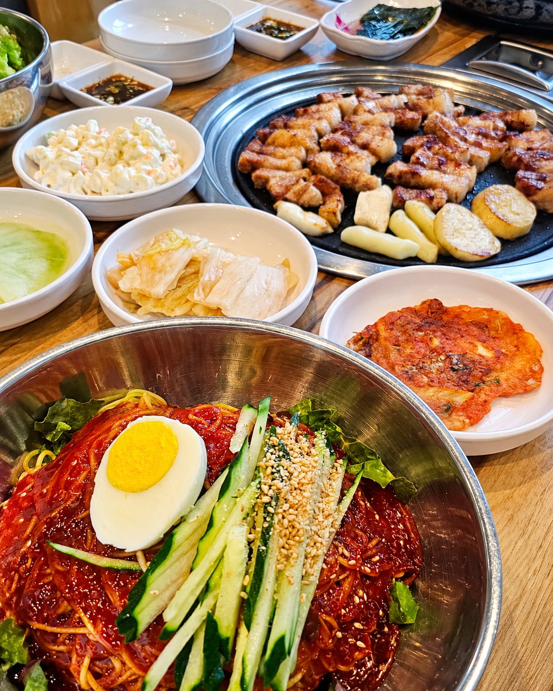 삶은 달걀과 오이, 깨를 올린 비빔냉면과 구운 삼겹살, 반찬